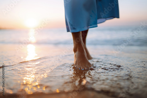 Close up of a female's bare feet walking at a beach at sunset. Summer time. Travel, weekend, relax and lifestyle concept.