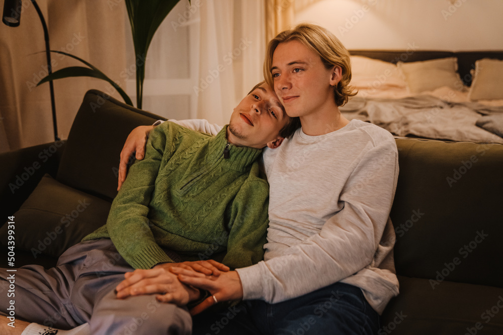 Obraz premium Young gay couple hugging and resting on couch while watching tv