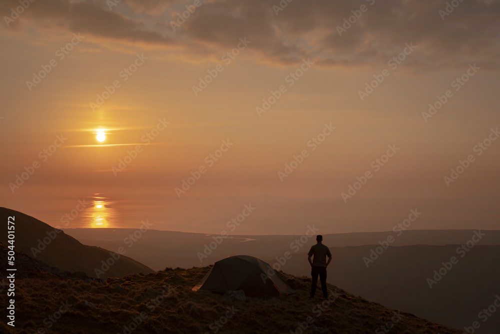 A man standing beside a wild camping tent at sunset in Snowdonia UK