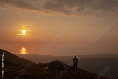 A man standing beside a wild camping tent at sunset in Snowdonia UK