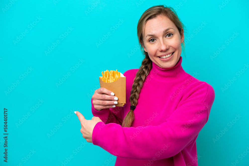 Young caucasian woman holding fried chips isolated on blue background pointing back Young caucasian woman holding fried chips isolated on blue background pointing back