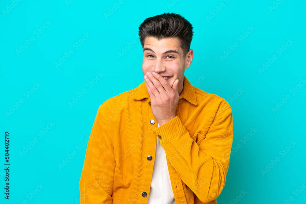 Obraz premium Young handsome caucasian man isolated on blue bakcground happy and smiling covering mouth with hand