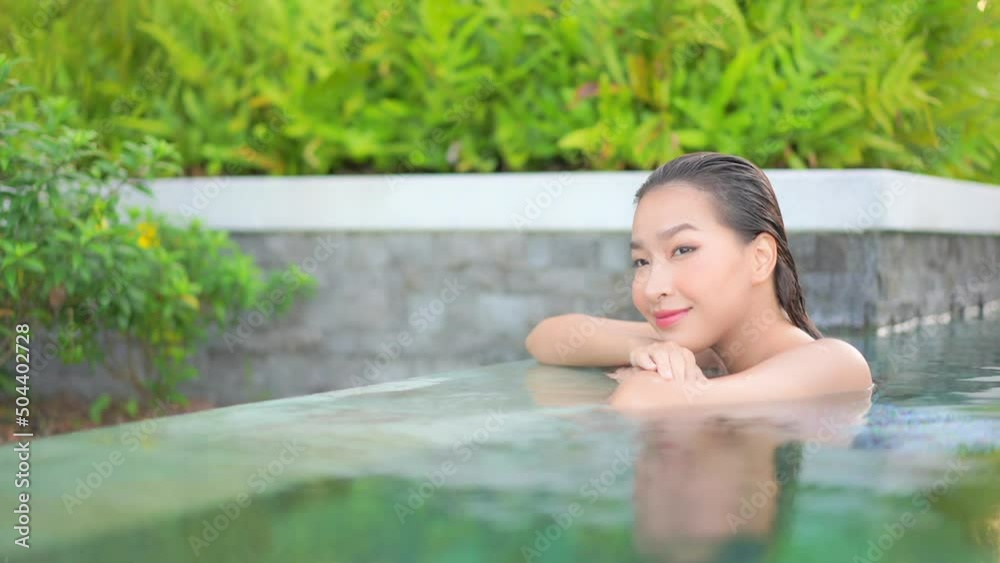 Close-up. A young, beautiful woman rests along the edge of a swimming pool while leaning her chin on her arms. Close-up. A young, beautiful woman rests along the edge of a swimming pool while leaning her chin on her arms.