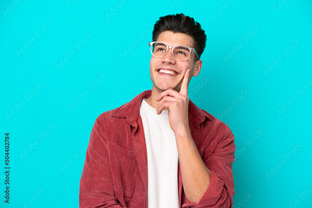 Young handsome caucasian man isolated on blue bakcground With glasses and thinking while looking up Young handsome caucasian man isolated on blue bakcground With glasses and thinking while looking up