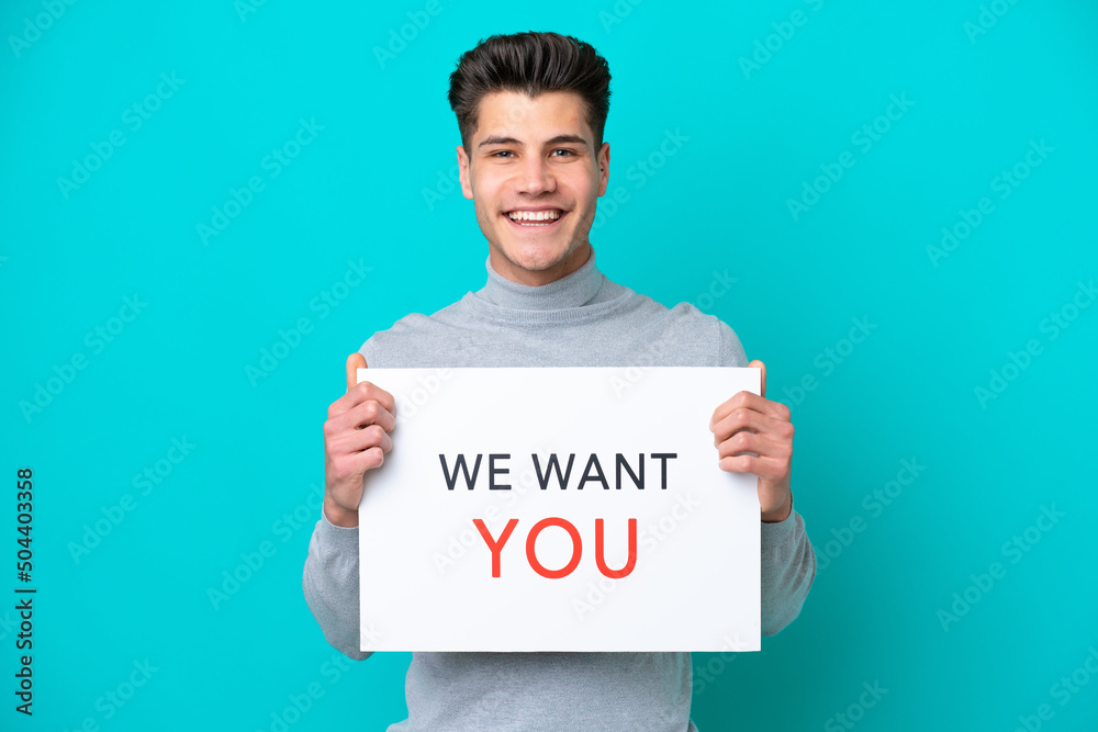 Young handsome caucasian man isolated on blue bakcground holding We Want You board with happy expression Young handsome caucasian man isolated on blue bakcground holding We Want You board with happy expression