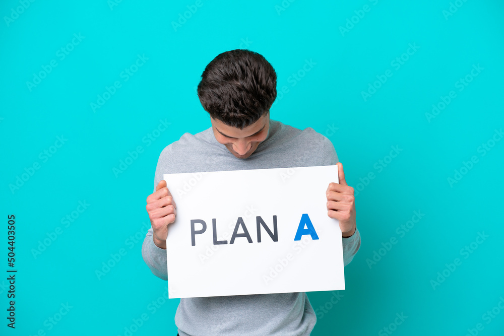 Young handsome caucasian man isolated on blue bakcground holding a placard with the message PLAN A Young handsome caucasian man isolated on blue bakcground holding a placard with the message PLAN A