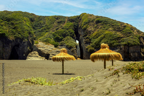 Beautiful empty secluded lonely sand beach,  thatch palapa umbrellas, crevice gap in rock (Iglesia de Piedra) - Cobquecura de la Loberia, Chile photo