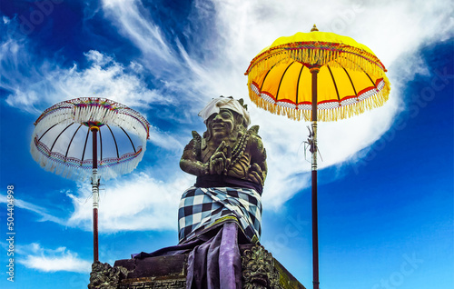 Balinese hindu mythological lord shiva stone figure between two traditional ceremonial umbrellas (tedung), blue sky white clouds - Bali, Ubud photo