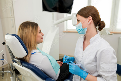 A female dentist is talking to a patient sitting in a dental chair.