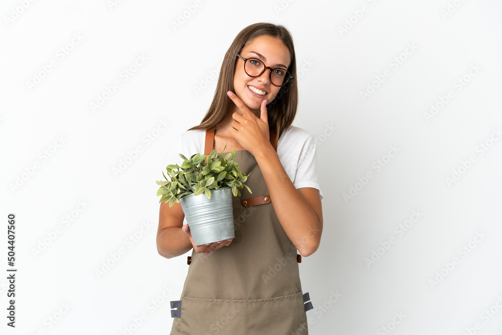 Gardener girl holding a plant over isolated white background happy and smiling Gardener girl holding a plant over isolated white background happy and smiling