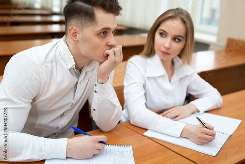Young couple of students, a guy and a girl, sit at a desk at a lecture and hold hands.