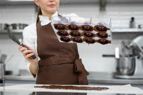 Chef or chocolatier makes sweet chocolates in a professional kitchen. She turns the mold over and pours the rest of the chocolate onto the table photo