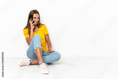 Young girl sitting on the floor keeping a conversation with the mobile phone with someone