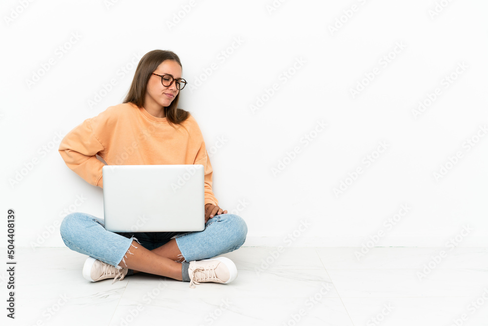 Young woman with a laptop sitting on the floor suffering from backache for having made an effort Young woman with a laptop sitting on the floor suffering from backache for having made an effort