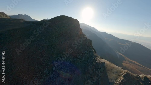 Aerial panorama view extreme man running on stone peak of high mountain at sunset sunrise natural glare. FPV sports drone speed male runner enjoy freedom winner discovery exploration on cliff top 4k photo