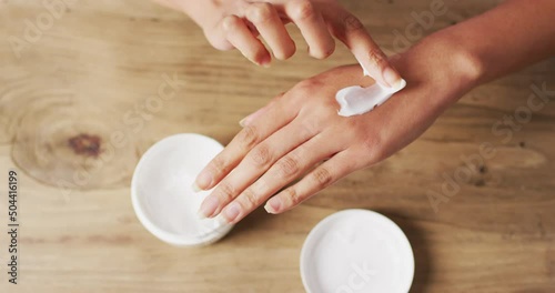 Video of hands of caucasian woman moisturizing hands with cream on wooden surface photo