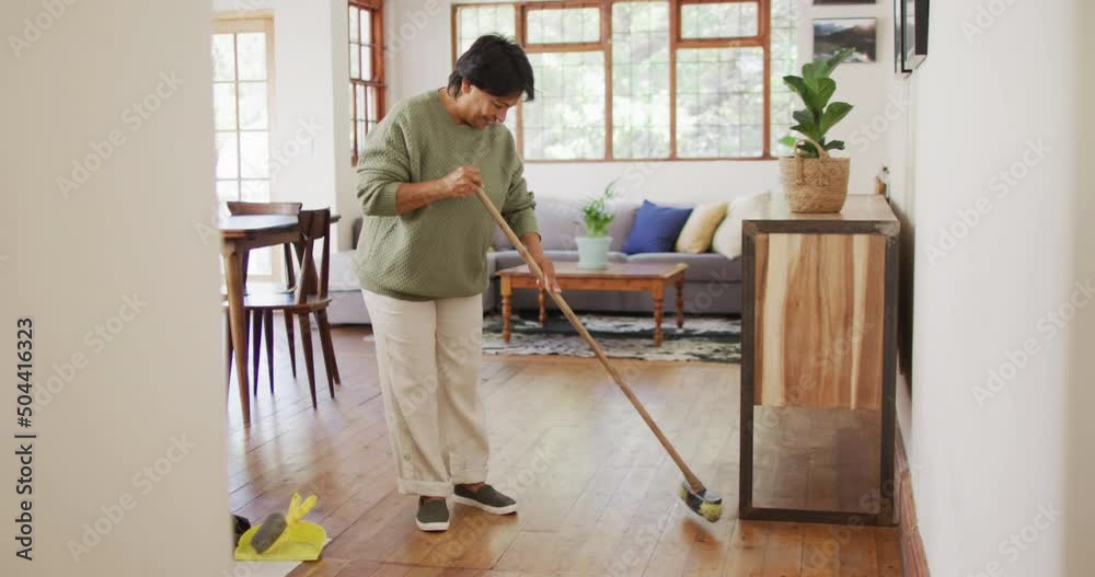 Smiling senior biracial woman cleaning floor in living room alone Smiling senior biracial woman cleaning floor in living room alone
