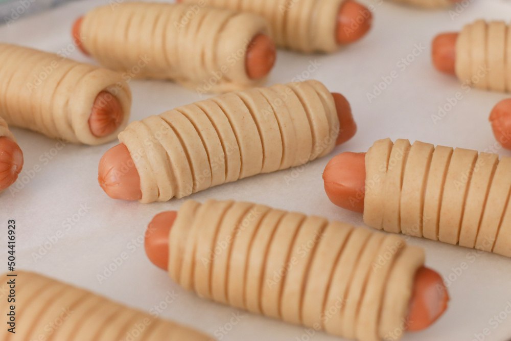 An uncooked sausage bread roll or hotdog bun dough on a baking tray to proving and resting before bake. A bread made of a mix of flour, milk, water, sugar, salt, active dry yeast, and butter An uncooked sausage bread roll or hotdog bun dough on a baking tray to proving and resting before bake. A bread made of a mix of flour, milk, water, sugar, salt, active dry yeast, and butter