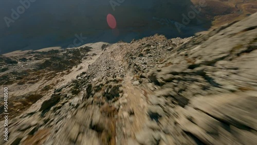 Aerial view speed dive cliff stone structure flying over mountain ridge at sun lights glare sunrise sunset. FPV sports drone shot picturesque rocky canyon hilly terrain wild scenery clear blue sky