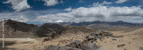 Sajama National Park surrounded by snow-capped mountains with wite clouds and sunshine surrounded by dry vegetation.