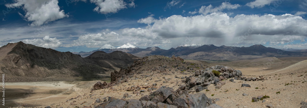 Sajama National Park surrounded by snow-capped mountains with wite clouds and sunshine surrounded by dry vegetation.