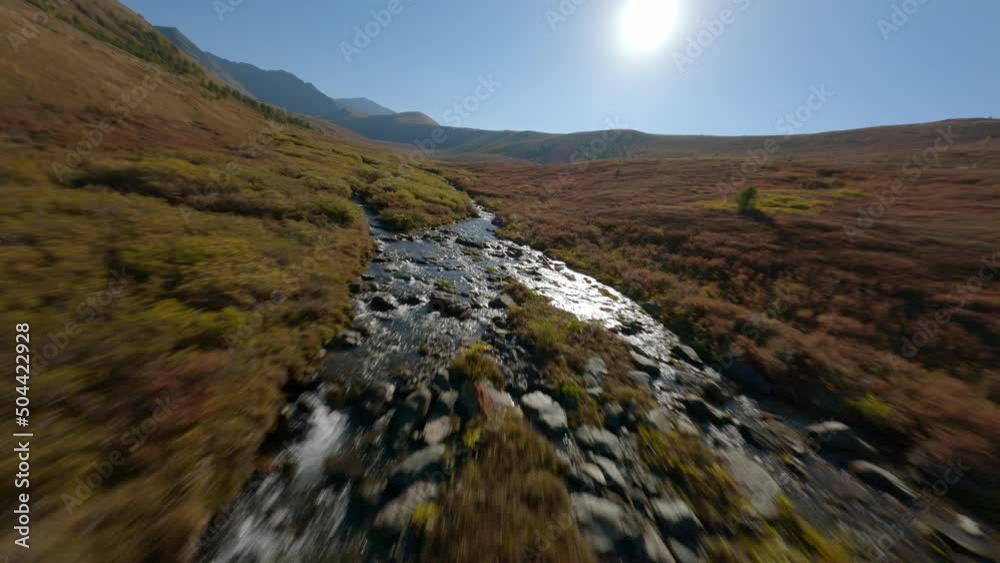FPV sports drone speed flight over natural mountain river water stream autumn spring landscape sun glare. Aerial view helicopter flying hilly terrain cliff valley bushes plant vegetation environment FPV sports drone speed flight over natural mountain river water stream autumn spring landscape sun glare. Aerial view helicopter flying hilly terrain cliff valley bushes plant vegetation environment