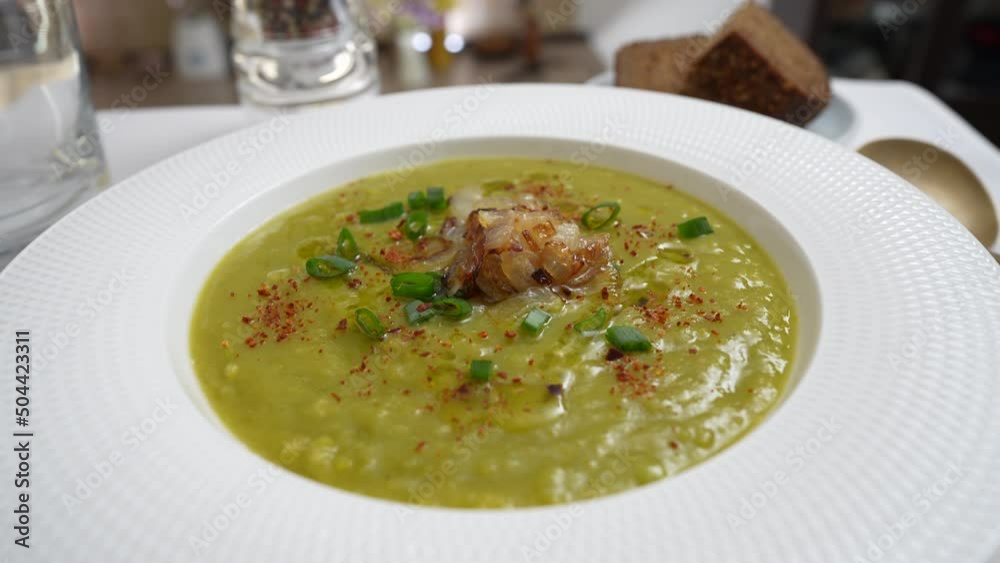 Green pea cream soup in white plate with spices on the table, rotate, close up. Healthy food, delicious dried green pea soup Green pea cream soup in white plate with spices on the table, rotate, close up. Healthy food, delicious dried green pea soup