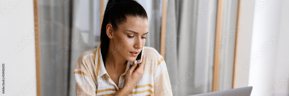 White brunette woman talking on cellphone and working with laptop White brunette woman talking on cellphone and working with laptop