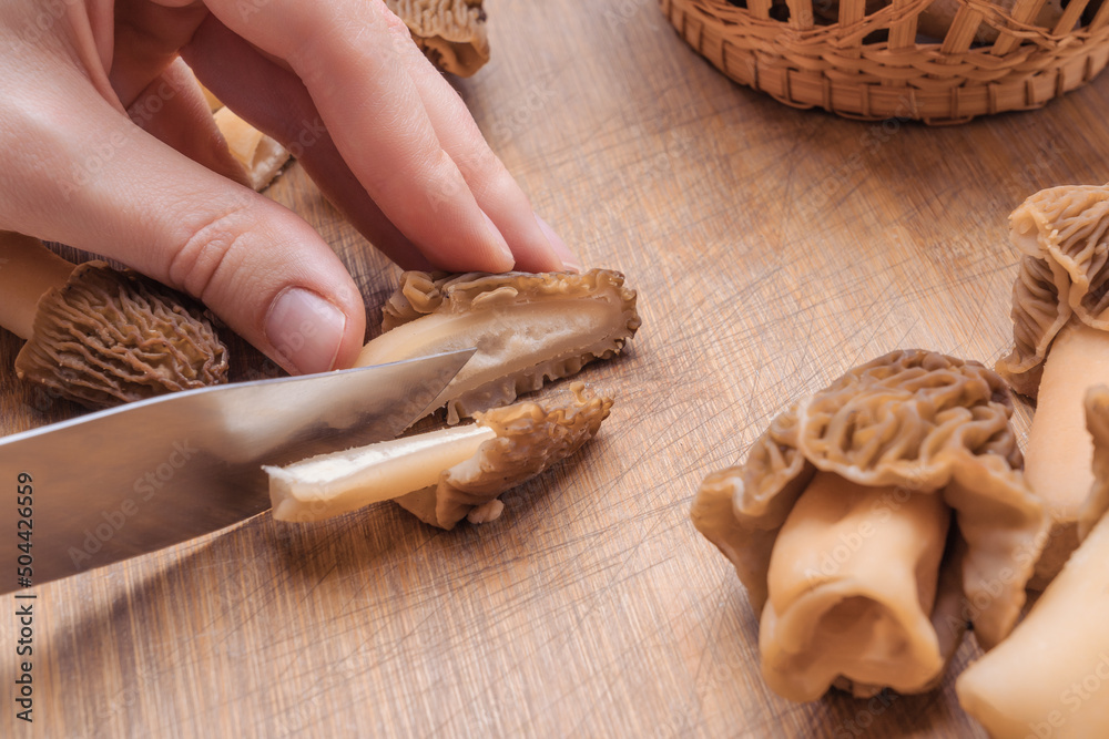 Cook slices morel mushrooms on a chopping board, close-up Cook slices morel mushrooms on a chopping board, close-up
