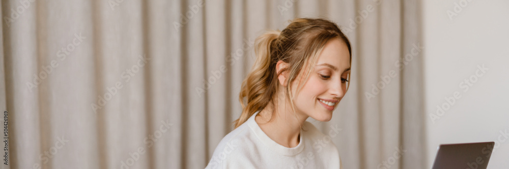 Young woman working with laptop and smiling in bedroom at home Young woman working with laptop and smiling in bedroom at home