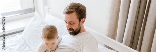 White father and son reading book while lying on bad at home