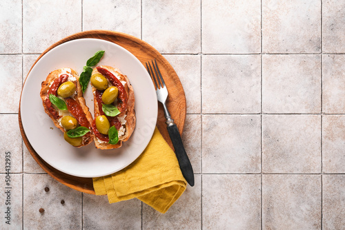 Bruschetta with sun dried tomatoes. Toast or sandwich with ricotta, sun dried tomatoes and Provence herbs with basil servered on a plate on a grey old cracked tile table. Top view banner menu recipe. photo