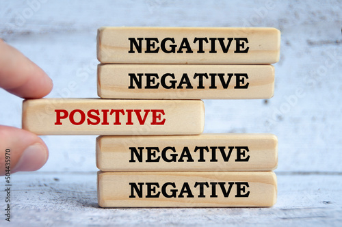Negative and positive text on wooden blocks with hand placing a wooden block in the middle.