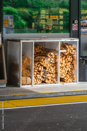 Sale of firewood at a gas station in Europe, a box with bundles of firewood on the street in front of a shop window with a reflection of the green leaves of the tree, fuel for fireplaces and barbecues