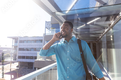 Smiling african american business traveler talking on smartphone walking at airport corridor