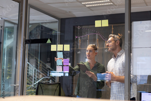 Confident caucasian colleagues planning strategy together seen through glass wall in workplace