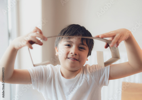 Happy young boy using cardboard for headphone, Active Kid with big smile while playing cardbox, Positive child relaxing at home on weekend, DIY Recyling toys idea for Children photo