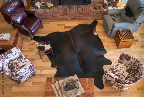 Furniture arrangement in living room with ranch cowboy western theme. Cowhide rug is near brick fireplace. Overhead view of central part of great room includes wood floor, cedar chest and horse statue