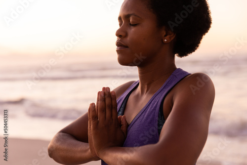 Midsection of african american mature woman with eyes closed meditating in prayer pose against sea
