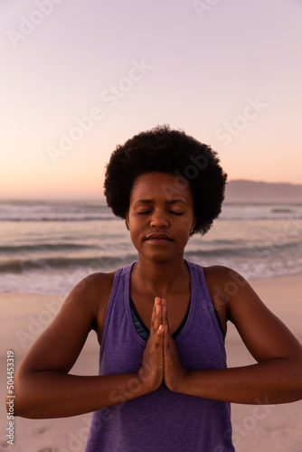 African american mature woman with eyes closed meditating in prayer pose against sea and clear sky