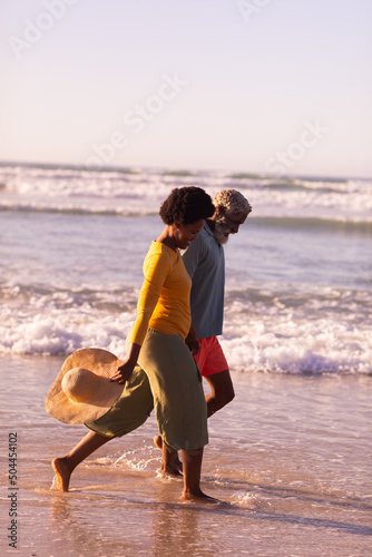 Side view of happy african american couple walking at shore against clear sky at sunset, copy space