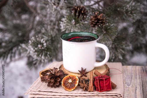 Ceramic cup with mulled wine and spices on the background of a snow-covered pine tree.