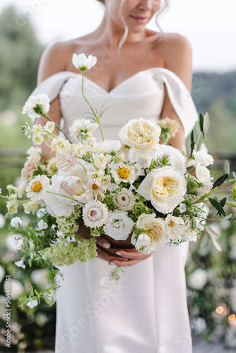 bride in a white wedding dress holding a bouquet of roses, peonies and greenery
