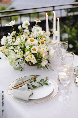 Banquet table is decorated with plates, cutlery, glasses and flower arrangements