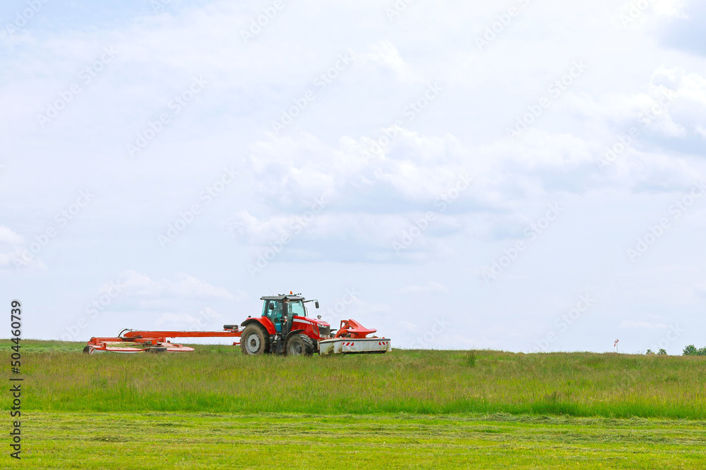 A red tractor mows the grass on a farmer's field. Two mowers will mow a large area of the field. A red tractor mows the grass on a farmer's field. Two mowers will mow a large area of the field.