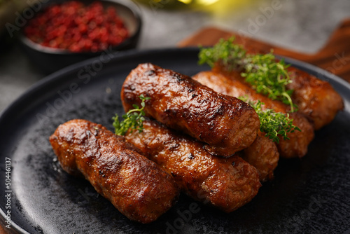 Traditional south european skinless sausages cevapcici made of ground meat and spices on black plate on dark wooden board, with thyme and watercress salad photo