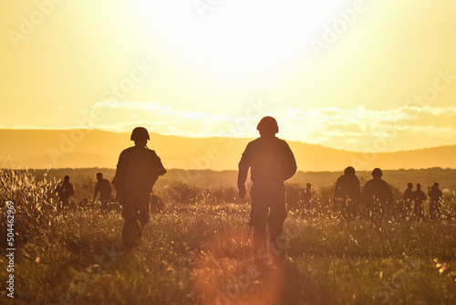 Bild auf Leinwand Dos soldados caminan por una pradera con montañas durante el atardecer