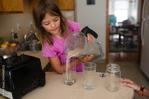 child pours green smoothie into cups