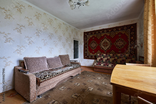 Example of Old Soviet Russian poor interior in Khruschev House. Aged  sideboard, table, chairs. Shabby floor. Tattered wallpaper on the wall. Apartment of pensioners. Selective focus. photo