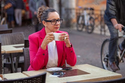 portrait of business woman in pink jacket drinks coffee in street cafe
